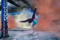 Girl practicing yoga at outdoor stage against colorful smoke — Stock Photo