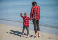 Vater und Sohn gehen Händchen haltend am Strand entlang — Stockfoto