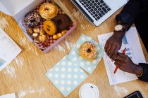 Cropped overhead view of cake box of doughnuts on woman's desk — Stock Photo