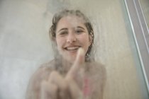Ritratto di giovane donna in doccia che attinge a una porta di vetro vaporizzata — Foto stock
