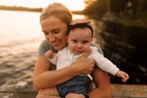 Mutter sitzt auf Seebrücke und umarmt kleine Tochter — Stockfoto