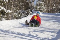 Man and son tobogganing in winter forest — Stock Photo