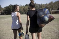 Mulheres em campo de futebol carregando bolas de futebol em saco líquido — Fotografia de Stock