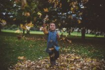 Девушка в парке бросает осенние листья — стоковое фото