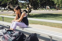 Colegiala sentada en el banco en el campo de deportes de la escuela - foto de stock