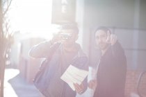 Two men in street, mid adult man looking through camera, young man pointing ahead — Stock Photo