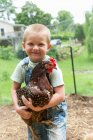 Мальчик с пятнистой курицей смотрит в камеру и улыбается. — стоковое фото