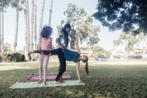 Girls and teenage schoolgirls practicing yoga standing half moon pose on school playing field — Stock Photo