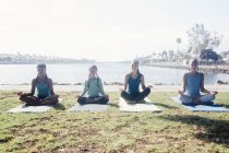 Alunas praticando ioga lótus posar ao lado do lago no campo de esportes da escola — Fotografia de Stock