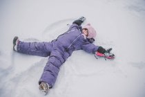 Молодая девушка делает снежного ангела в снегу — стоковое фото