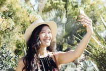 Young woman outdoors, taking selfie in ornamental garden — Stock Photo