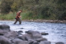 Vista lateral do homem vadear no rio com vara de pesca — Fotografia de Stock