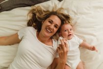 Overhead portrait of woman and baby daughter lying on bed — Stock Photo