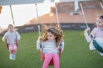 Girls at preschool, swinging on playground swings in garden — Stock Photo