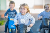 Niña y niños en preescolar, carreras de motos push en el jardín - foto de stock