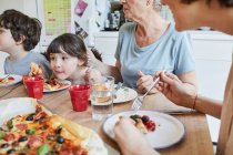 Сім'я трьох поколінь сидить за кухонним столом їсть піцу — стокове фото