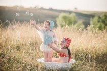 Duas garotas no campo, brincando na banheira de plástico de água — Fotografia de Stock