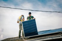 Two workmen installing solar panels on roof of house, low angle view — Stock Photo
