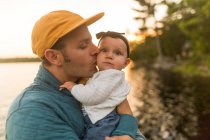 Мужчина целует маленькую дочь на берегу озера — стоковое фото