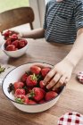 Jeune garçon prenant des fraises dans un bol, section médiane, gros plan — Photo de stock