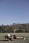 Frau auf Fußballplatz macht Liegestütze mit Fußball — Stockfoto