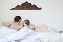 Madre sentada en la cama con la niña - foto de stock