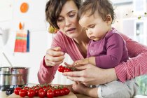 Mother and baby daughter in kitchen sorting tomatoes — Stock Photo