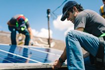Three workmen installing solar panels on roof of house, low angle view — Stock Photo