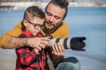 Padre e hijo al aire libre, padre enseñando a su hijo a usar la cámara - foto de stock