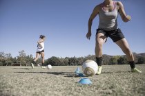 Dos mujeres jóvenes regateando balones de fútbol en el campo de fútbol - foto de stock