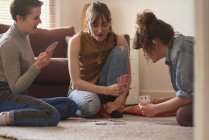Amis jouant aux cartes sur le sol dans le salon — Photo de stock