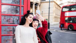 Два молодих стильних жінок, що приймають selfie бласть червоний телефон, Лондон, Великобританія — стокове фото