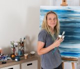 Portrait of mature female artist with abstract canvas  in studio — Stock Photo
