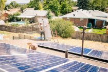 Arbeiter, der Sonnenkollektoren auf dem Dach des Hauses installiert, trägt Sonnenkollektoren, Rückansicht — Stockfoto