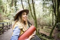 Young woman in trilby looking up from forest footbridge — Stock Photo