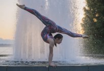 Teenage girl beside fountain balancing on hands in yoga position — Stock Photo