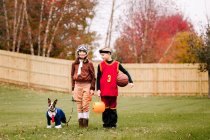 Porträt von Junge, Zwillingsschwester und Boston Terrier in Halloween-Kostümen im Garten — Stockfoto