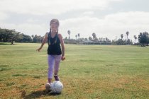 Écolière donnant des coups de pied ballon de football sur le terrain de sport scolaire — Photo de stock