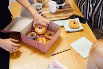 Imagem cortada de mulher colocando donuts em caixa de bolo — Fotografia de Stock