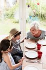 Nonna seduta al tavolo della cucina con nipote e nipote, sorridente — Foto stock