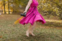 Молода жінка з фотоапаратом танцює в парку — стокове фото