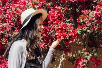 Jovem mulher ao ar livre, olhando para flores coloridas penduradas — Fotografia de Stock