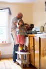 Mädchen trinkt auf Stuhl, während Vater in Küche Essen zubereitet — Stockfoto