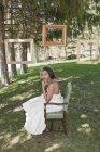Portrait of bride in wedding dress sitting in chair outdoors — Stock Photo