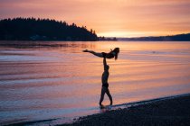 Пара практикує йогу на пляжі на заході сонця — стокове фото