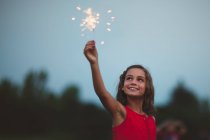Girl with arm raised holding sparkler — Stock Photo