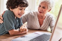 Бабуся і онук сидять за столом, використовуючи ноутбук — стокове фото