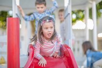 Girl at preschool, lying at top of playground slide in garden — Stock Photo