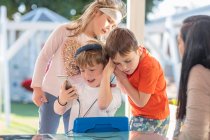 Троє маленьких дітей, використовуючи смартфон, слухають навушники — стокове фото