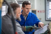 Male car mechanics pointing at clip board in repair garage — Stock Photo